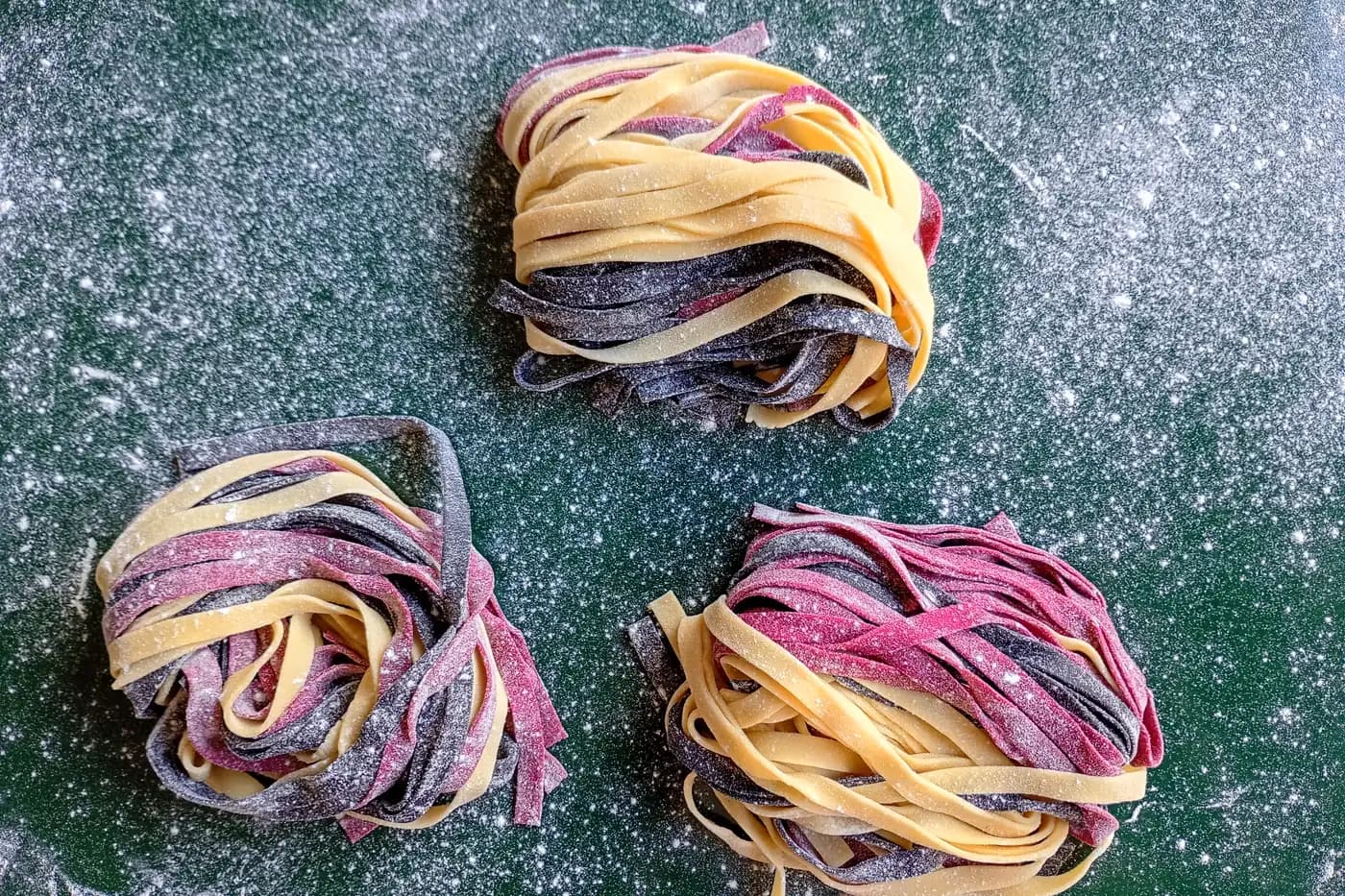 Nidos de tallarines caseros de colores sobre la mesada enharinada
