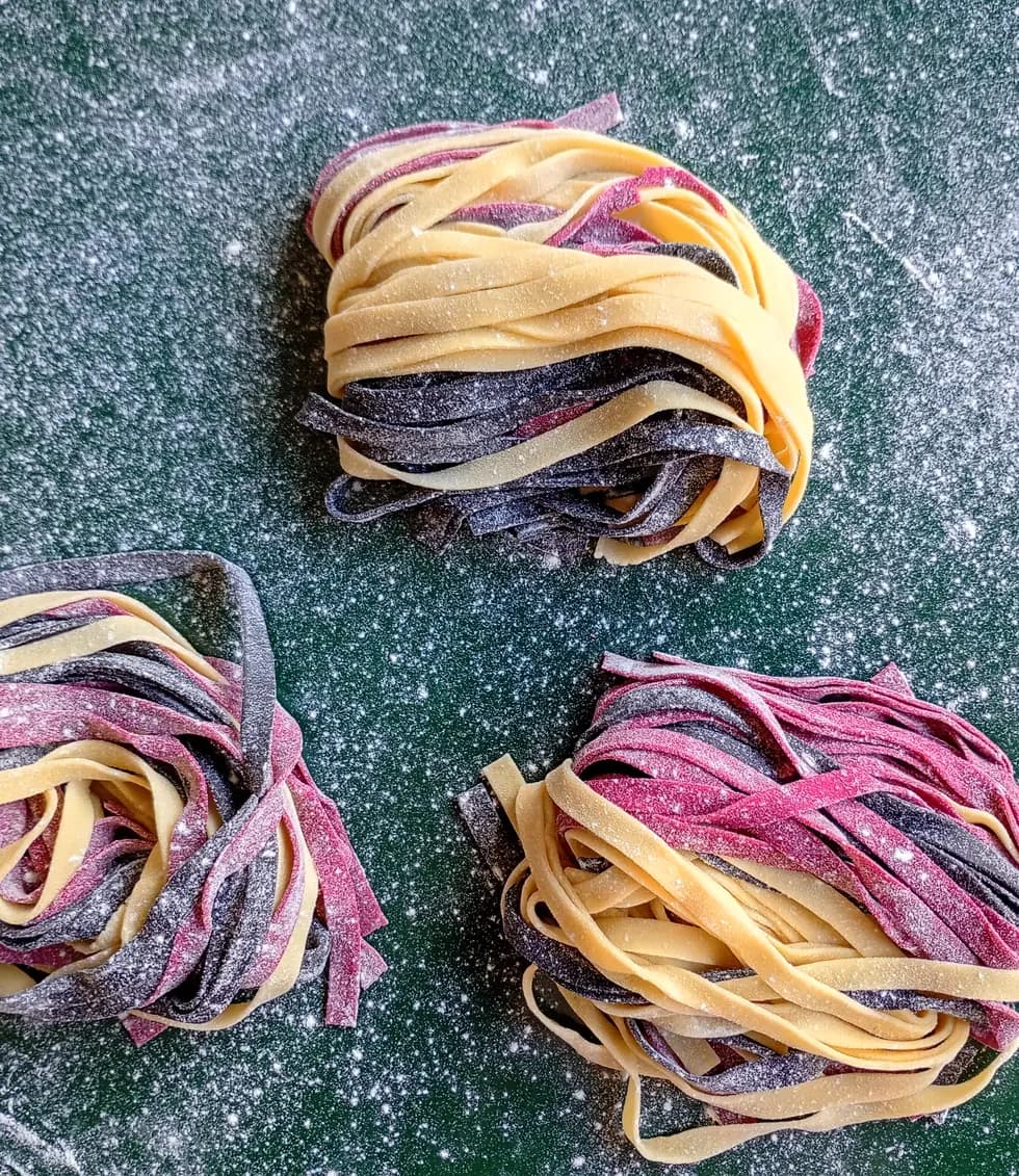Tres nidos de tallarines caseros de remolacha y al huevo sobre la mesada enharinada